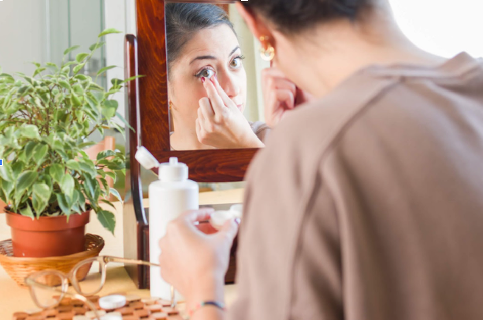 woman wearing contact lenses while looking in mirror