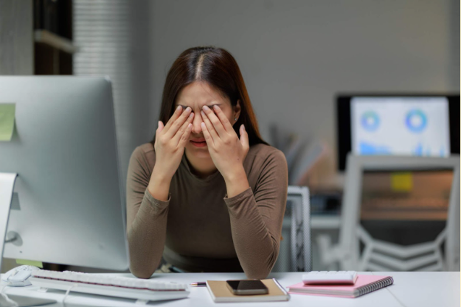 Woman experiencing eye strain and fatigue while working on a computer in an office